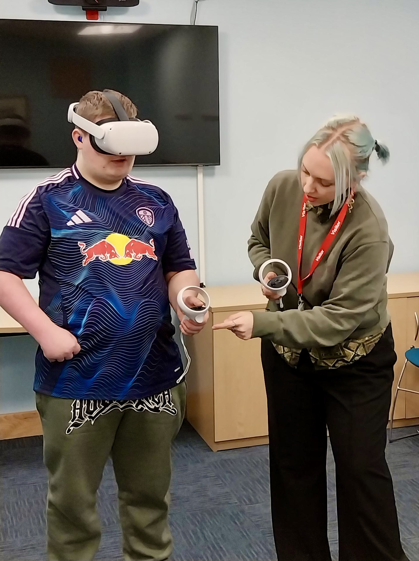 A young man wears a VR headset with the researcher standing nearby giving instructions