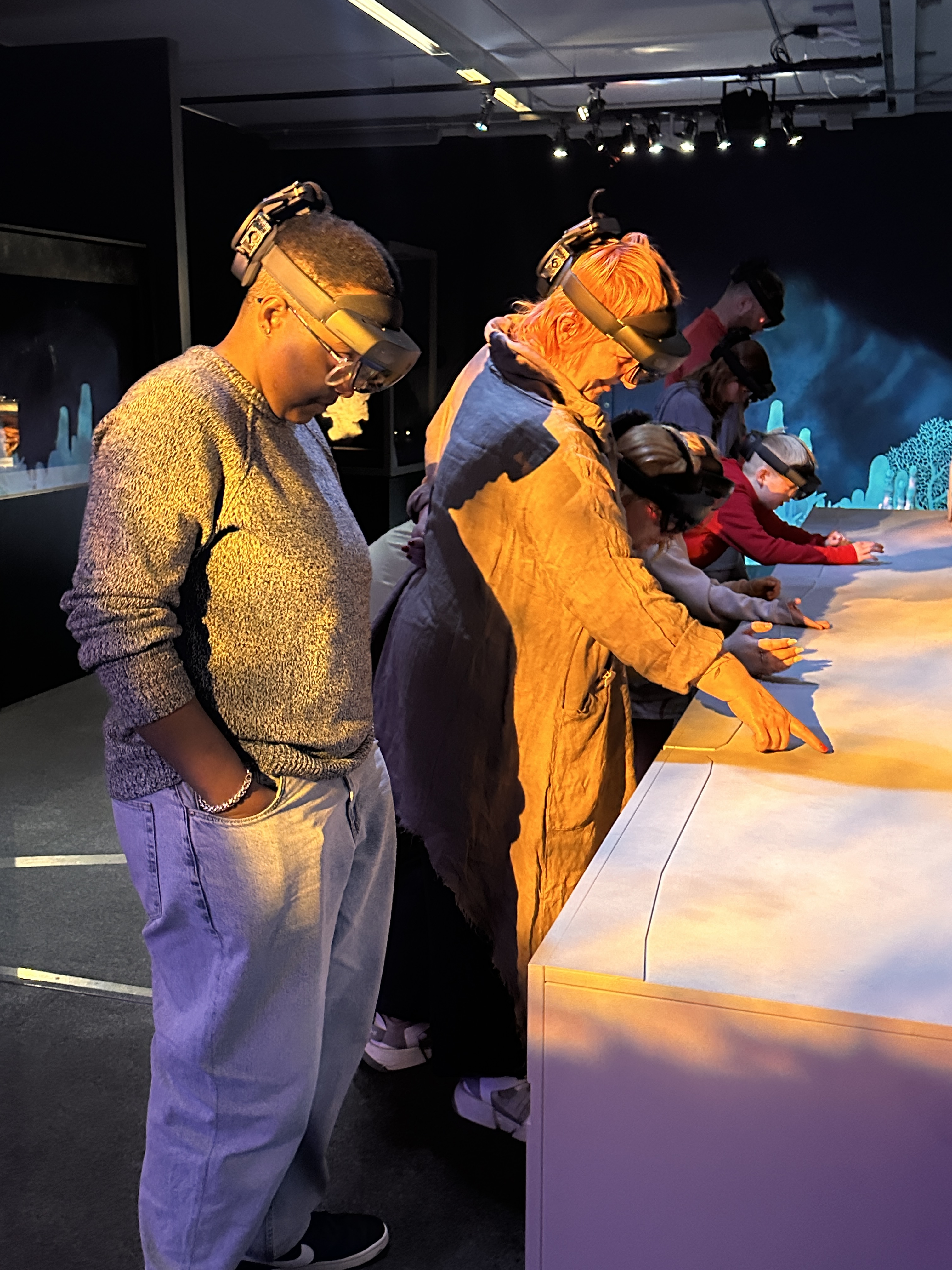 People in a gallery wearing augmented reality headsets reach outwards