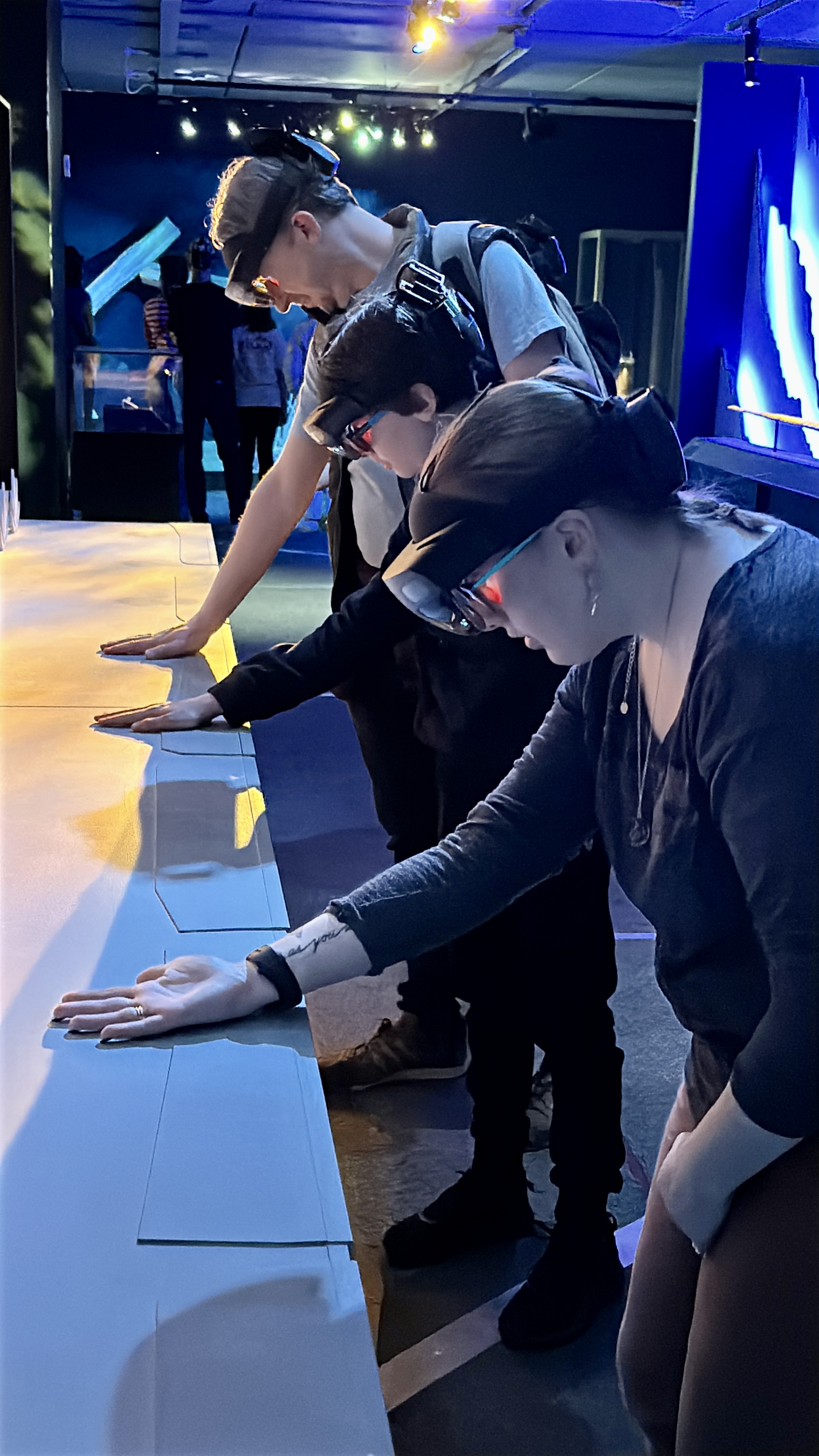 Three people wearing mixed reality headsets reach their hands forward